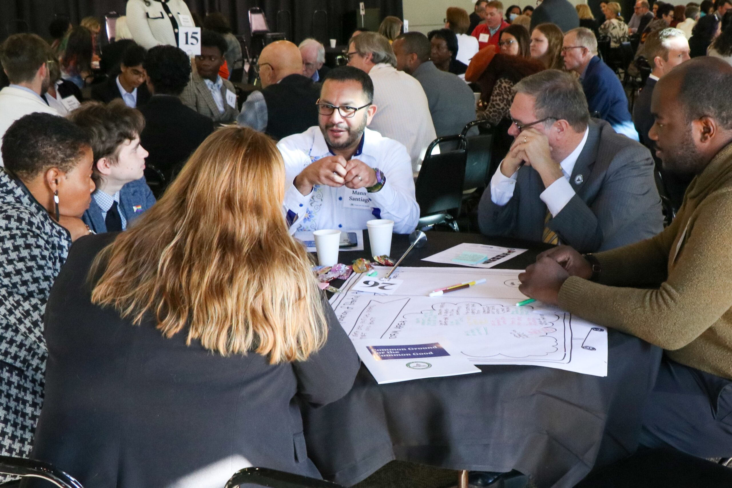 A group of civic leaders engages in discussion while seated at a table